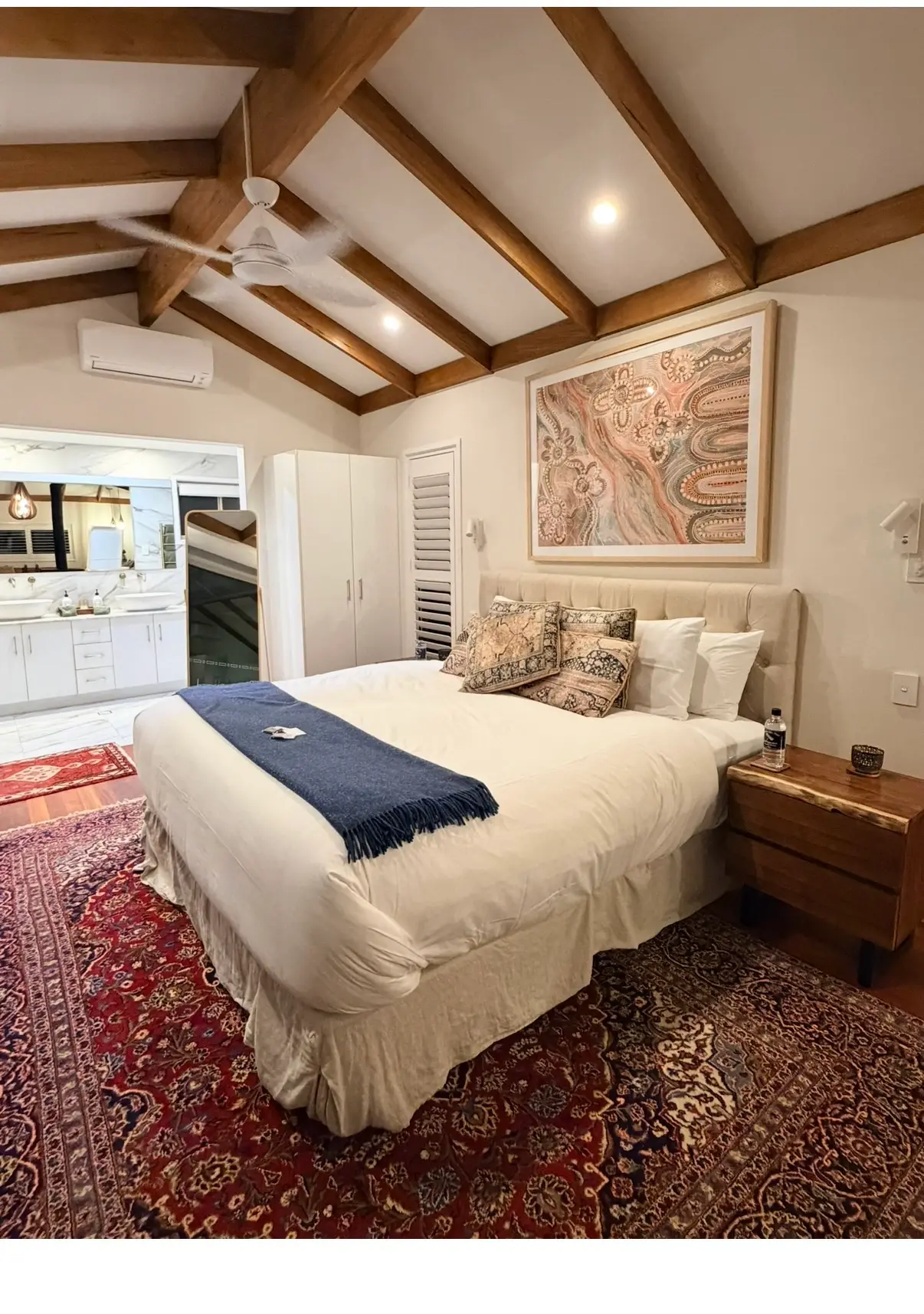 A calm bedroom with warm timber beams and artwork