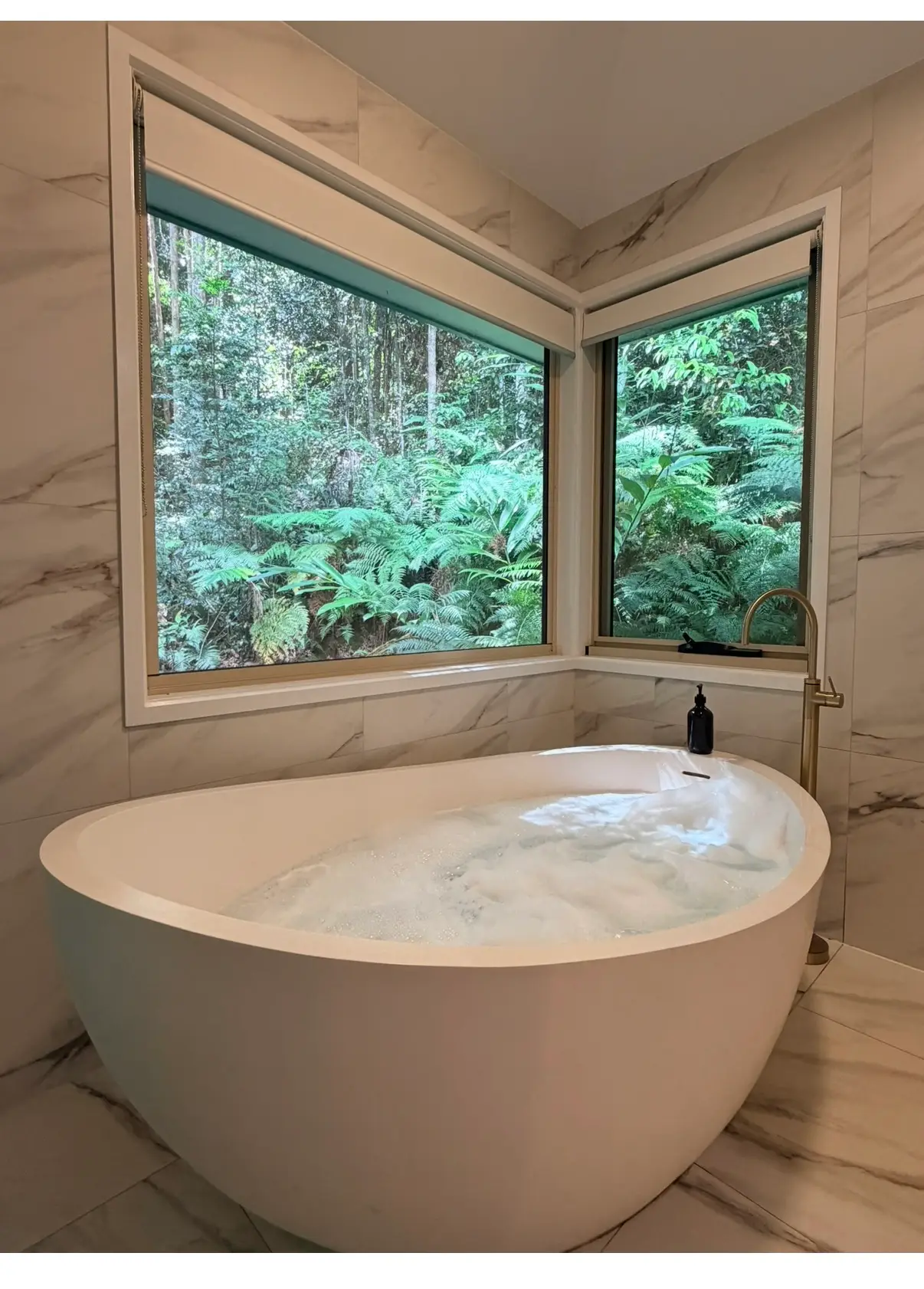 Oval spa bath beside corner windows opening onto rainforest ferns at Narrows Escape